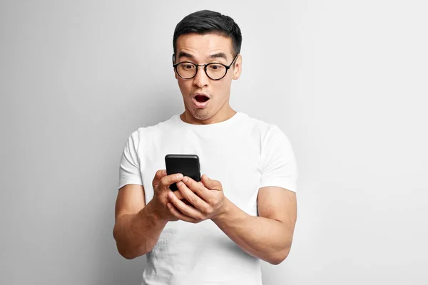 Pohledný Asijský Chlápek Bílém Studiu Vypadá Překvapeně Obrazovce Mobilního Telefonu — Stock fotografie