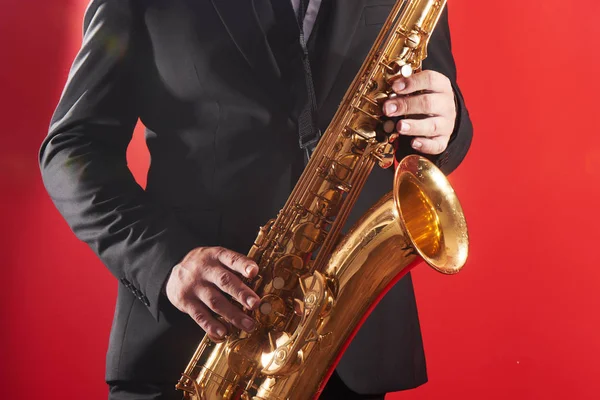 穿着西服的职业音乐家萨克斯风手的肖像在萨克斯风上演奏爵士音乐 在摄影棚里演奏红色背景 — 图库照片