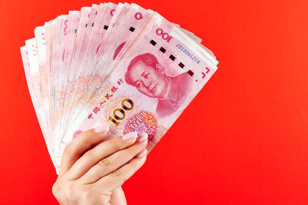 A pile of RMB banknotes of Chinese yuan money in a female hand on a red background