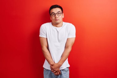 Şaşkın Asyalı karar veremez, şüpheler, ne yapacağını ya da söyleyeceğini bilmiyor. Utangaç bir poz belirsiz Kazak kırmızı stüdyo arka planda size bakar