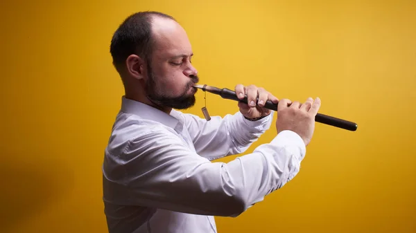 Professional musician man playing a pipe closeup in a yellow studio. Folk wind instrument, flute