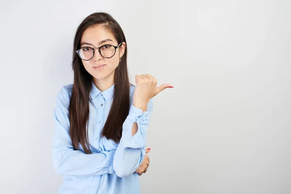 Asian Kazakh girl student with glasses shows finger on empty copy space, place for your advertisement on white background isolated