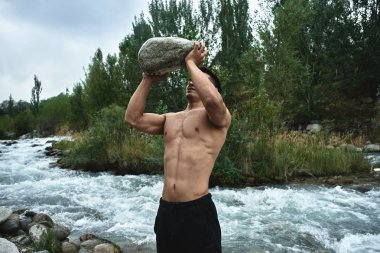 Kazak kaslı atlet adam trenler ve doğada nehir tarafından egzersizleri. Asyalı yakışıklı açık havada aşırı fitness egzersiz yok