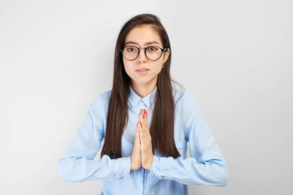 Asian kazakh girl student with glasses and shirt in prayer thanksgiving pose keeps hands together on white background isolated