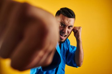 Mavi kimono üniformalı Asya Kazak karate savaşçısı izole kopya alanı ile sarı arka plan üzerinde kamera yumruklar