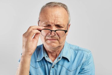 Görme problemleri. Yaşlı bir adam gözlüklerini çıkarıyor. Tatmin olmadım. Beyaz gömlekli yaşlı vatandaş. Optik