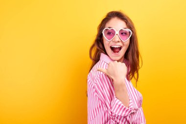 Heyecanlı yüz sarı stüdyoda rahat izole giyinmiş kız şaşırttı. Kazak kadın kitabe üzerinde parmak gösterir, ürününuz için ücretsiz kopya alanı