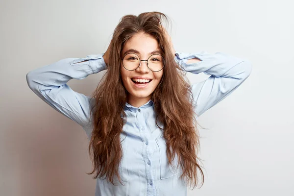 Portrait of Asian Kazakh student girl with long brunette hair and glasses laughing and holding her head in a white studio