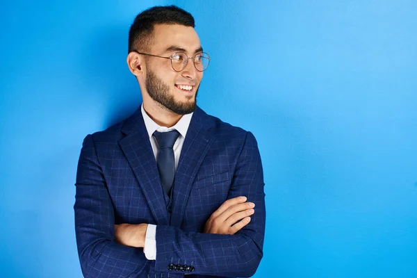 Portrait of smiling handsome successful kazakh asian businessman in suit with arms crossed on blue studio background , isolated with copy space