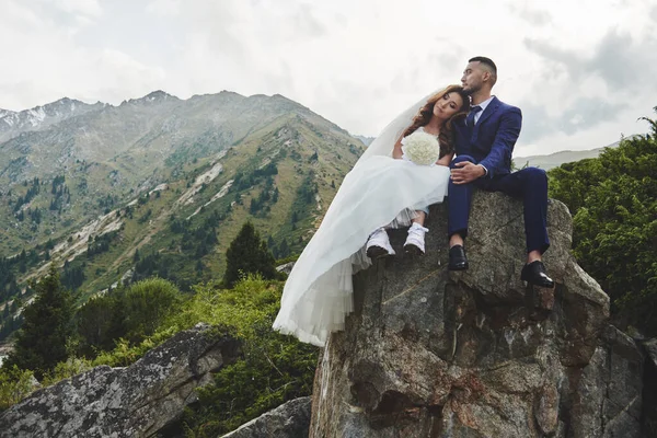 Beautiful wedding photo on mountain lake. Happy Asian couple in love, bride in white dress and groom in suit are photographed against background of the Kazakh landscape