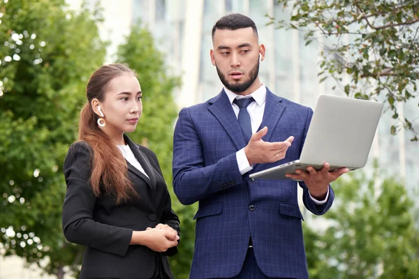 Businessman and businesswoman realtors with laptop outside, asian kazakh entrepreneurs discuss project