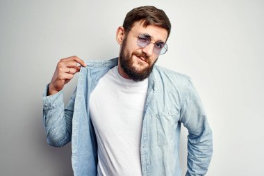 Moda görünümlü beyaz yakışıklı gözlüklü seksi adam havalı poz veriyor ve el kol hareketi yapıyor gömleğinin altında beyaz tişört, stüdyoda izole edilmiş duygusal ifade yüzlü.