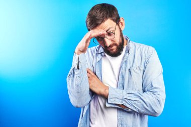 Yakışıklı beyaz adam başını tutuyor, iş yerinde sürekli stres, baş ağrısı ve duygusal çöküntü yaşıyor, ofis çalışanı mavi arka planda kopya alanı ile izole edilmiş.
