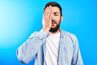 Sıradan giyinmiş beyaz sakallı bir adam mavi stüdyo geçmişine izole edilmiş bir yüz hareketi yapıyor. Başarısızlık, ezik, konsepti izlemek acıtır.