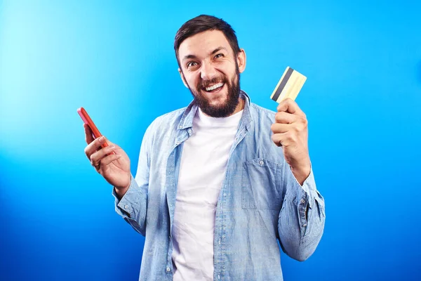 手に携帯電話とクレジットプラスチックカードで成功した笑顔ハンサムな髭の男は インターネットを介して購入やサービスのために支払う — ストック写真