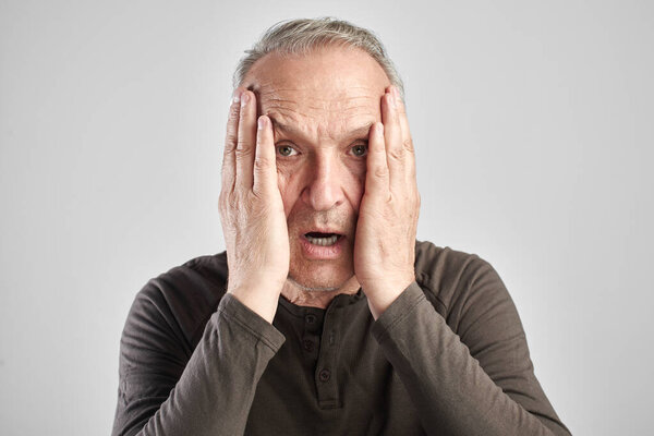 Shocked surprised senior citizen fearfully closes face with hand isolated on white background, human emotions concept