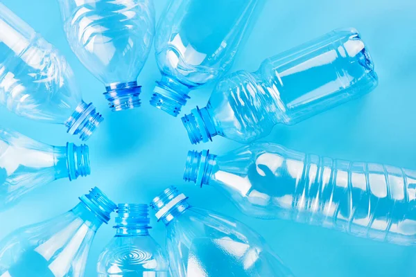 Set of empty different type water bottles lie isolated on blue background, top view. Plastic production and processing concept