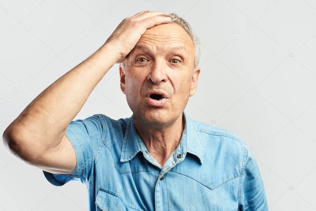 Confused gray-haired elderly man clutching his head in panic isolated in white studio. OMG, what have I done, made a mistake
