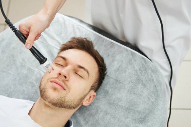 Güzellik uzmanı kadın güzellik salonunda genç bir adam için yaşlanma karşıtı yüz gerdirme ameliyatı yapıyor.