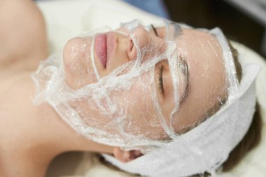 Doktor kozmetik uzmanı güzellik salonunda genç ve çekici bir kadına yüz temizleme prosedürü uyguluyor. Yaz bakımı