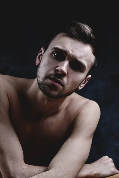 深刻な顔と暗い壁に対して裸の胴を持つ感情的な若いUnshvenブルネットの男のアートポートレート — ストック写真