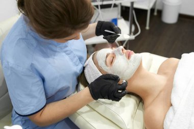 Doktor kozmetik uzmanı güzellik salonunda genç ve çekici bir kadına yüz temizleme prosedürü uyguluyor. Yaz bakımı