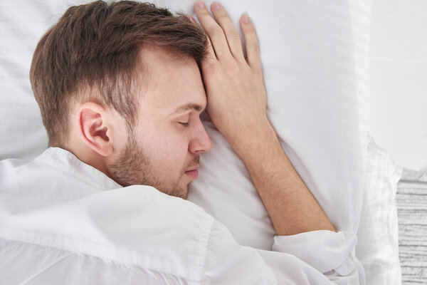 Close-up portrait of sleeping brunette man on white pillow