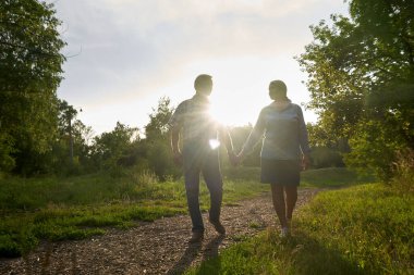 Bir yaz parkında romantik bir randevuya çıkmış yaşlı bir çift yeşil ağaçların arkasında gülümsüyor ve sarılıyor.