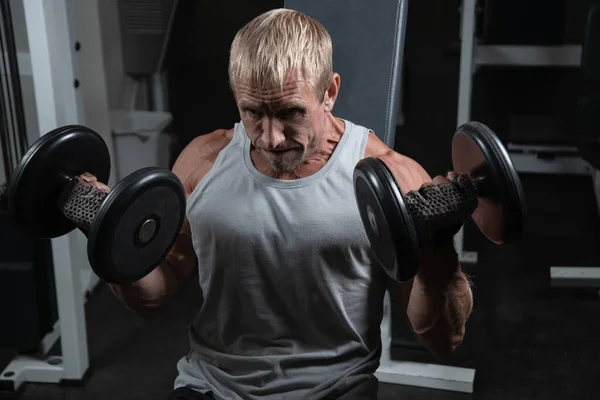 Homens maduros fazendo exercícios de supino inclinado com halteres na  academia