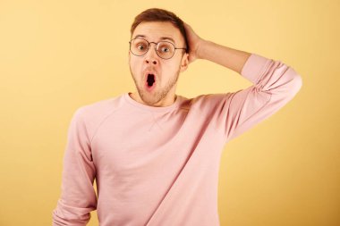 Şok olmuş adamın portresi ağzı açık şaşırmış, duygusal beyaz yüzlü, pembe günlük kıyafetler giymiş sarı arka planda izole edilmiş.