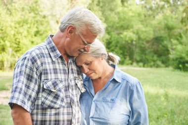 Yaz parkında romantik bir buluşmada, yeşil ağaçların arka planında gülümseyen ve sarılan yaşlı çiftlerin yakın plan portresi.