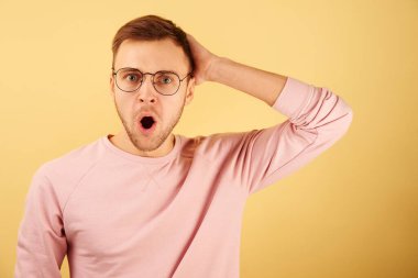 Şok olmuş adamın portresi ağzı açık şaşırmış, duygusal beyaz yüzlü, pembe günlük kıyafetler giymiş sarı arka planda izole edilmiş.