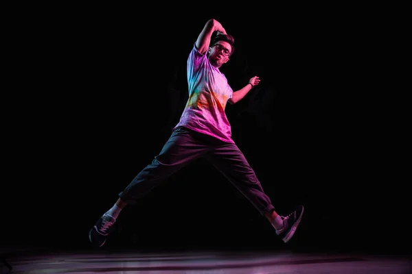 Professional break dancer jumping, practicing modern hip-hop dance in pink neon light