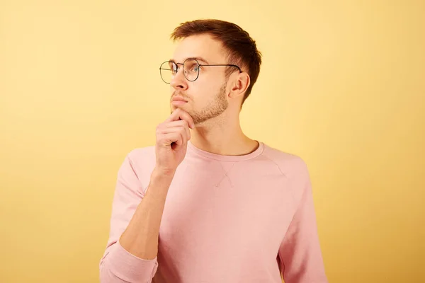 ピンクのカジュアルな黄色の背景に隔離された服を着て 雛と思考を保持し 普及した顔をした眼鏡をかけて男の肖像画 — ストック写真