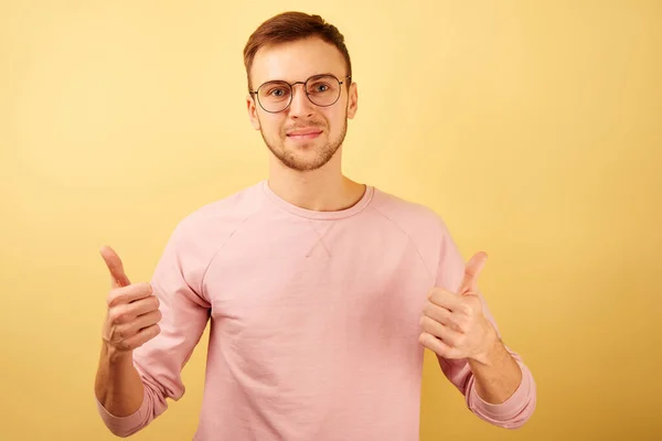 ピンクのカジュアルな服で黄色の背景に単離された親指を示す笑顔の顔を持つメガネを身に着けている白人男性の肖像画を閉じる — ストック写真