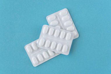 Mavi arka planda beyaz plastik pakette bir sürü ilaç ve ilaç var. Sağlık hizmetleri kavramı.
