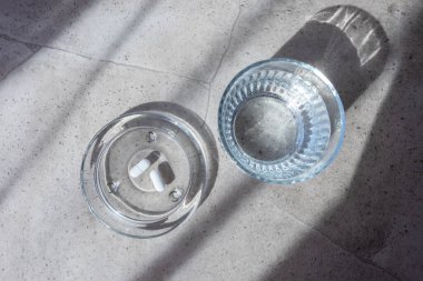 Pill and glass with water on the stone table. Healthcare from pharmacy. Person sit at home because of illness.