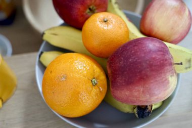 Bir masada, ağzına kadar elma, olgun portakal, taze muz ve sulu nar gibi çeşitli meyvelerle dolu bir kase vardır.