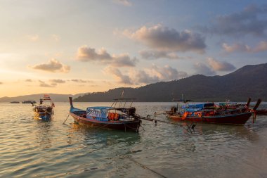 Lipe Island, Tayland, kumsalda üzerinde dramatik günbatımı ile geleneksel longtail tekne ön planda.