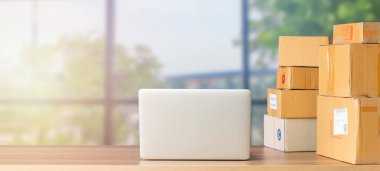 İş yerindeki dizüstü bilgisayar, küçük işletme sahibi. Müşteriye teslim etmek için karton kutu dolusu ürün. Çevrimiçi satış, e-ticaret, paketleme konsepti, sabah ışığı, evden çalışma, bulanık görüntü.