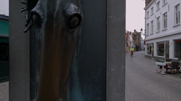 Camera Slides Horse Head Fountain Reveal Cyclist Narrow Brugge Street — Stock Video