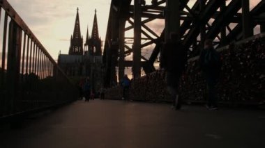 Kamera güneş batmadan olarak Hohenzollernbrucke Köln Katedrali Almanya'ya karşı geçiş yayalar ile yükselir.