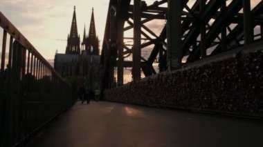 Kamera güneş batmadan olarak Hohenzollernbrucke Köln Katedrali Almanya'ya karşı geçiş yayalar ile yükselir.