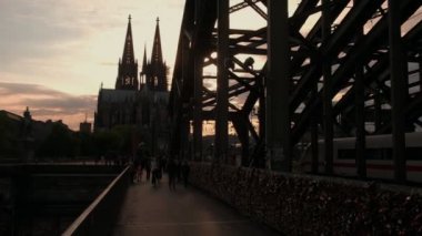 Kamera güneş batmadan olarak Hohenzollernbrucke Köln Katedrali Almanya'ya karşı geçiş yayalar ile iner.