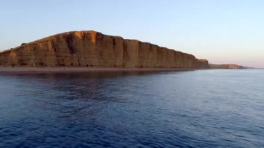 Drone düşük deniz üzerine sinekler sonra kayalıklarla ve beach West Bay Dorset'deki / daki doğru yükselir. Altın saat sırasında vurdu. 