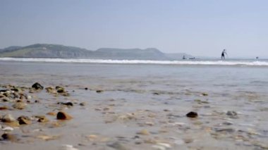 Sandy Beach Lyme Regis sörfçü çıkıyorum olarak üzerinde düşük düzey slayt. Cliffs Jurassic Coast arka planda görülmektedir