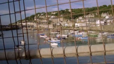 Mousehole Cornwall Limanı demirleyen renkli balıkçı tekneleri ile ortaya çıkarmak için çitin arkasından kamera yükselir
