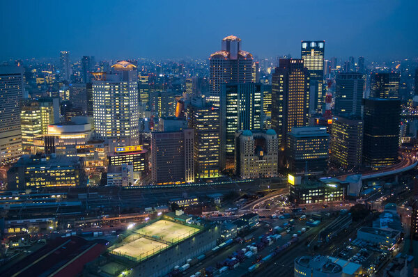 The blue hour in the Japanese city of Osaka as seen from high up. The city lights are shining in the evening light
