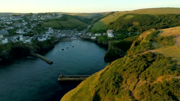 Drone flies sideways from cliffs with the village of Port Isaac behind in the golden light of dawn — Stock Footage Drone Flies Sideways Cliffs Village Port Isaac Golden Light Dawn Video Clip