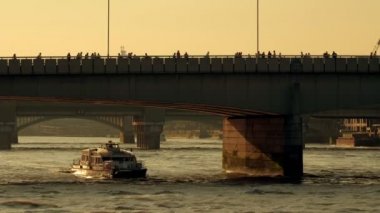 Thames Clipper nehir otobüsü Londra Köprüsü 'nün altında gün batımında geçer. Açık üst tur otobüsleri köprüyü geçip